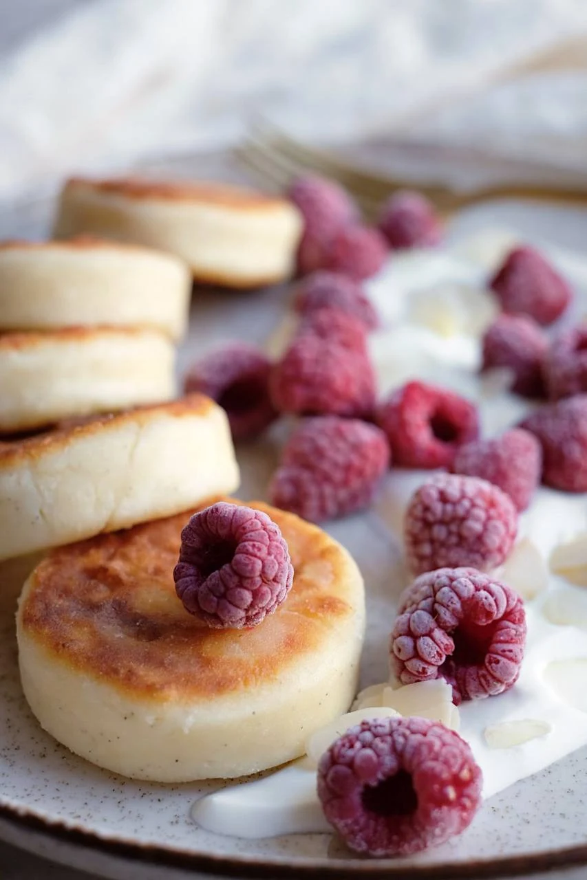 Homemade syrniki served with raspberries and cream